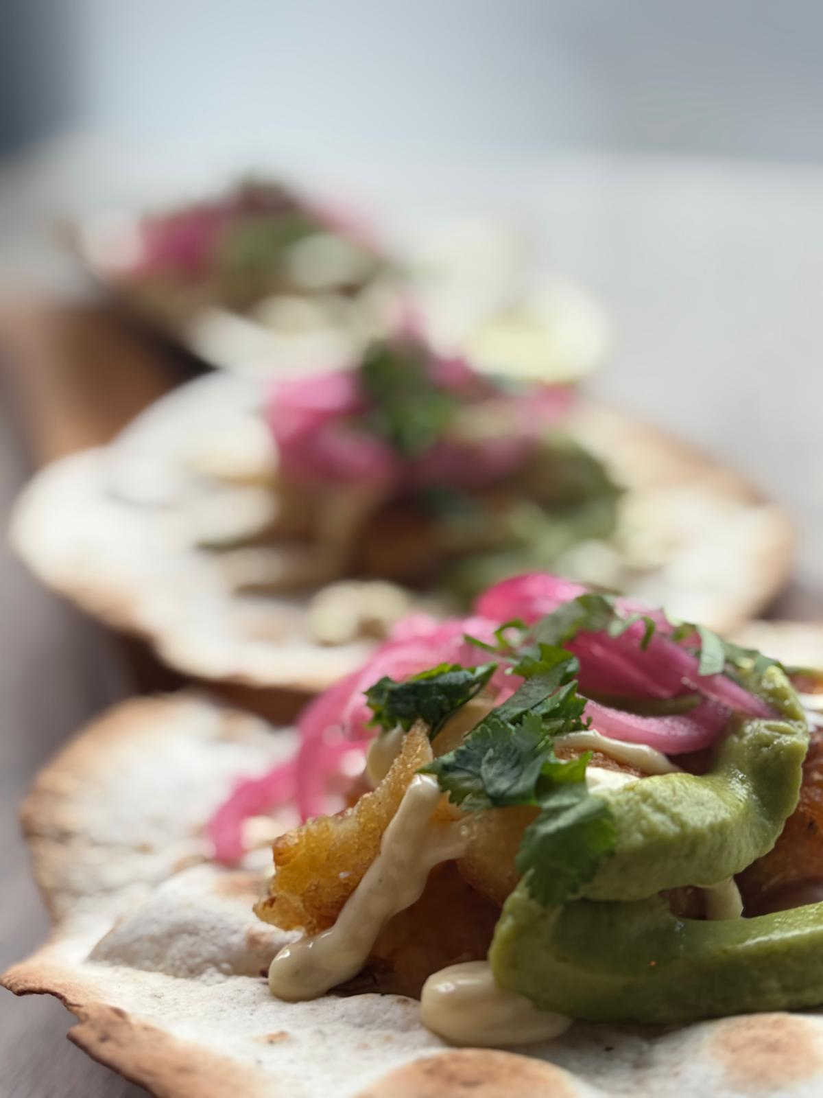 Crispy fish tacos on soft flour tortillas with avocado cream, chipotle mayo, pickled red onion and coriander